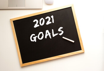 Text 2021 GOALS written in chalk on a slate board. Office desk.