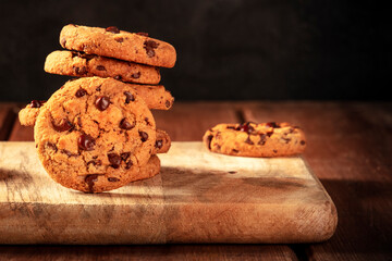 Chocolate chip cookies stack on a dark rustic wooden background, with a place for text