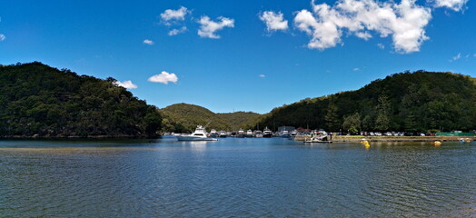 Beautiful view of a creek with boats, mountains, trees, blue sky with light clouds in the background, Bobbin Head, Ku-ring-gai Chase National Park, New South Wales, Australia
