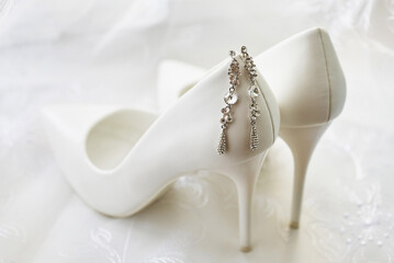 graceful earrings of the bride on the white leather shoes. wedding accessories. close-up, macro
