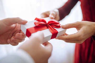 Valentine's day concept. A giftbox with red ribbon in hands. Loving couple give each other presents on 14 February. Romantic Boyfriend and girlfriend celebrating lover's day.