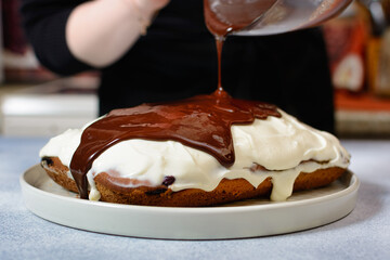 chef pours chocolate icing on the finished cake