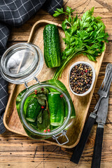 Obraz na płótnie Canvas Green salted cucumbers in a glass jar. Wooden background. Top view