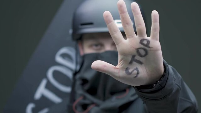 Close up of young man protester in helmet and mask showing on hand title stop, protests in USA