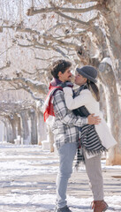Young couple hugging and kissing on a snowy winter park near of a many big trees full of snow. Concept of joint rest. Winter Photography 2021.