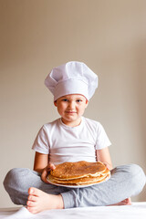 Photo shoot baby in white chef cap with pancakes on white background . Carnival Festival