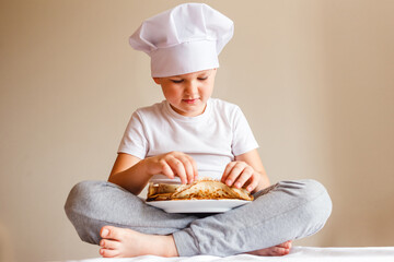 boy in a white T-shirt sits and finds pancakes on a white background. Carnival Festival