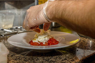 Serving the finished dish. Chef's hands close up. Chef puts soft cheese on slices of chopped tomatoes on a white plate