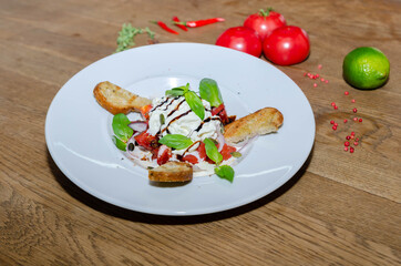 Salad with goat cheese, tomatoes, baguette on a white plate. Close-up