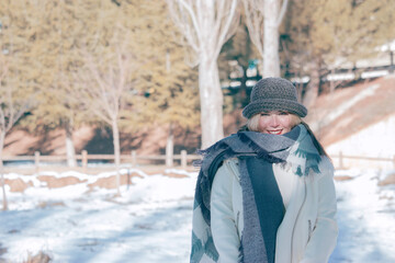 Attractive young woman smiling to the camera in wintertime outdoor with cozy warm clothes. She enjoys fresh nature in a sunny winter day. Winter output 2021.