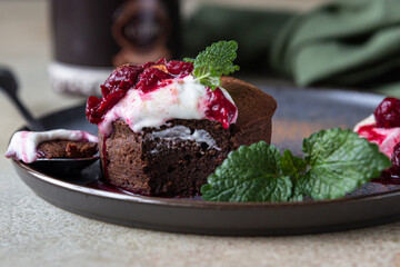 Mini chocolate cake or brownie with cream, cherry and mint on a ceramic plate. Chocolate fondant.