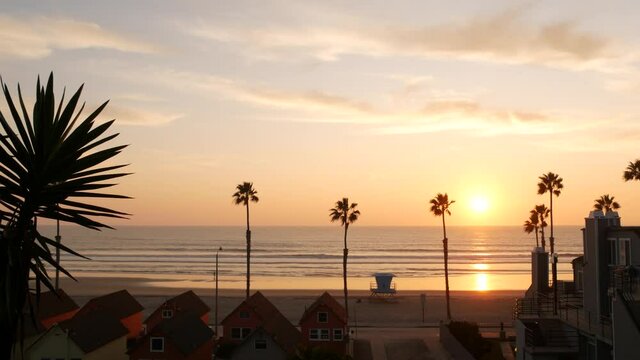 Palms silhouette sunset sky, California aesthetic. Oceanside USA. Tropical pacific ocean beach atmosphere. Los Angeles vibes. Lifeguard watchtower, palmtree and baywatch tower hut. Beachfront cottages