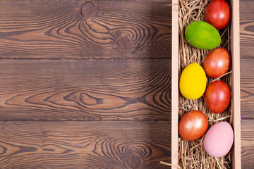 Colorful Easter eggs on a bed of straw in a long wooden box on a wooden table. Rustic style, copy space, flat ley