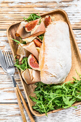 Sandwich with arugula, fig, prosciutto, Ciabatta and blue cheese on a wooden tray. White background. Top view