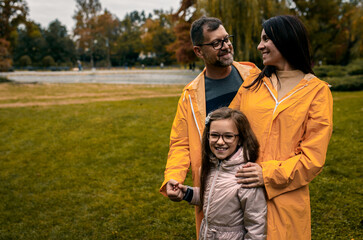 Family of three in raincoat enjoying together in city park.