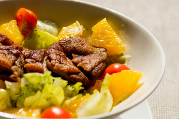 Roasted duck with fresh tomatoes, orange, herbs on a white plate. Close-up