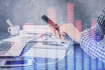 Double exposure of man's hands holding and using a digital device and forex graph drawing. Financial market concept.