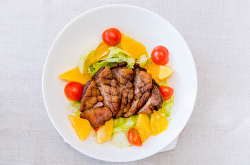 Roasted duck with fresh tomatoes, orange, herbs on a white plate. View from above