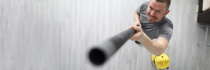 Happy man look up and smile at home. Person hold black hose from yellow vacuum cleaner in his hand...