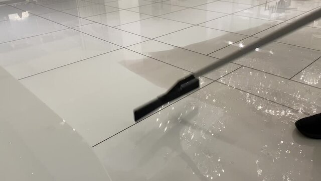 Cleaning a white marble floor with water and a large squeegee