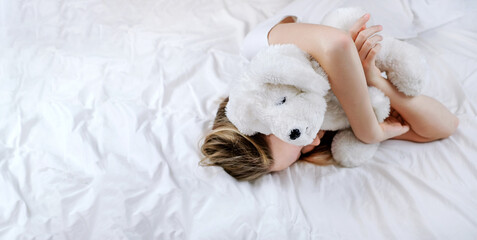 Little child girl hugs and sleeping in the bed with toy, enjoyng sweet dreams. Copy space