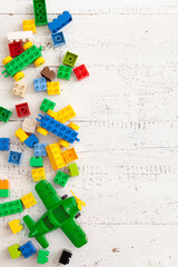 Developing multi-colored cubes on a white wooden background. Plastic construction toys. Top view of a green toy plane and other educational toys.