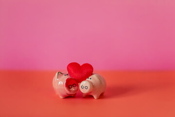 Two figurines of pigs and a red heart on a pink and red background. Composition for Valentine's...