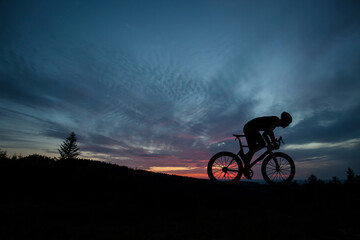 Fototapeta na wymiar The silhouette of the cyclist on bike at sunset.A man ride on bike on the mountains. Sport and active life concept sunset time. A man riding a bicycle in a nature.