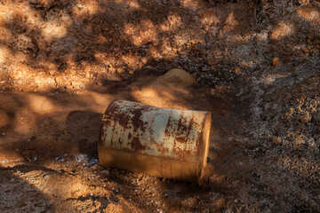 Rusty metal barrel sticking out of the brown soil against the dirty yellow clay. two rusty barrels...