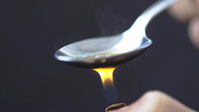 A close up view of a spoon with cooking heroin with a lighter