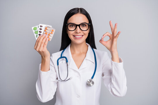 Photo of doctor lady hold pills show okey wear specs stethoscope white uniform isolated grey color background
