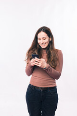 Cheerful young woman texting message on smartphone over white wall.