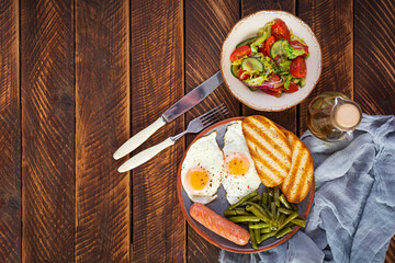 Breakfast with eggs, grilled sausage, green beans and toast on wooden background