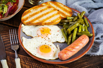 Breakfast with eggs, grilled sausage, green beans and toast on wooden background