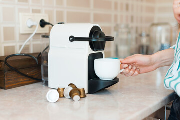 Close up photo of woman making coffee with capsule machine in kitchen.