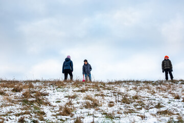 Low angle view of three children outdoor on a grassy snow hill with sky in the background.