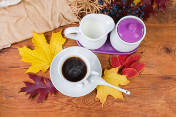 Coffee in cup, milk on rustic table among autumn leaves