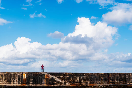 A single man stands on the harbour walls looking outwards towards the open sea and the vast expanse of a lovely sky.