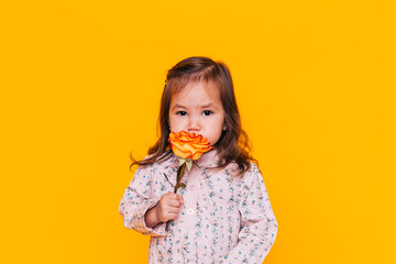 Child holding a flower in front of a yellow background. Valentine's Day. Mother's day