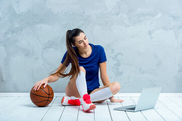 Young girl doing exercises with basketball ball watching online tutorials on laptop. A sports coach...