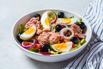 Tuna salad with egg, olives and vegetables in white bowl, white background. Diet food concept.