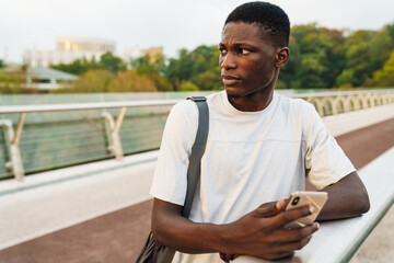 Focused african american guy using mobile phone on urban bridge