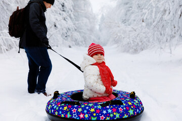 Young father pull little toddler girl on snow tube. Cute little happy child having fun outdoors in...