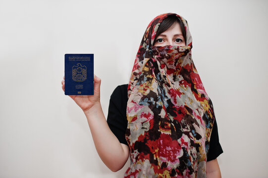 Young arabian muslim woman in hijab clothes hold United Arab Emirates passport on white wall background, studio portrait.