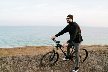 Handsome unshaven guy in sunglasses riding his bicycle on coast