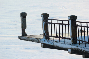 Detail of an old abandoned bridge with broken railing over a frozen river