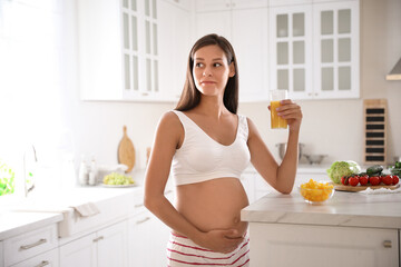 Fototapeta na wymiar Young pregnant woman with glass of juice in kitchen. Taking care of baby health
