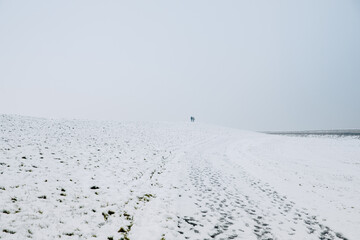 Fototapeta na wymiar Wide landscape with snow. Two people on the snow-covered dike. Snow on the North Sea 