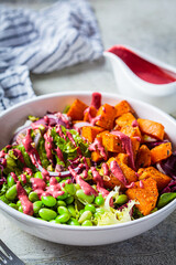 Vegan salad bowl with baked sweet potato, edamame beans, nuts and pink beetroot dressing. Vegan food concept.