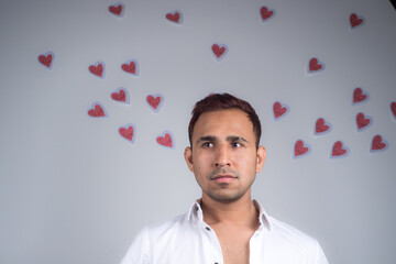 Young man dreaming and looking happy with many paper hearts flying behind him, white background. Concept of love, Valentine
